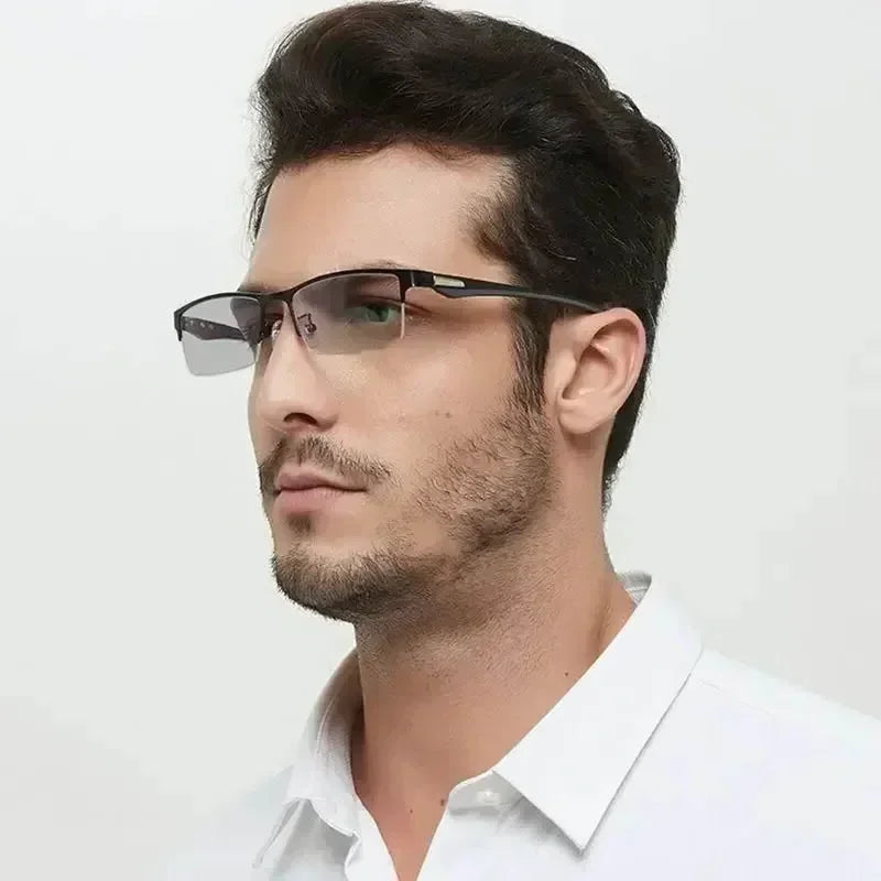 Un homme portant des lunettes de lecture photochromiques noires et une barbe courte, regardant sur le côté.