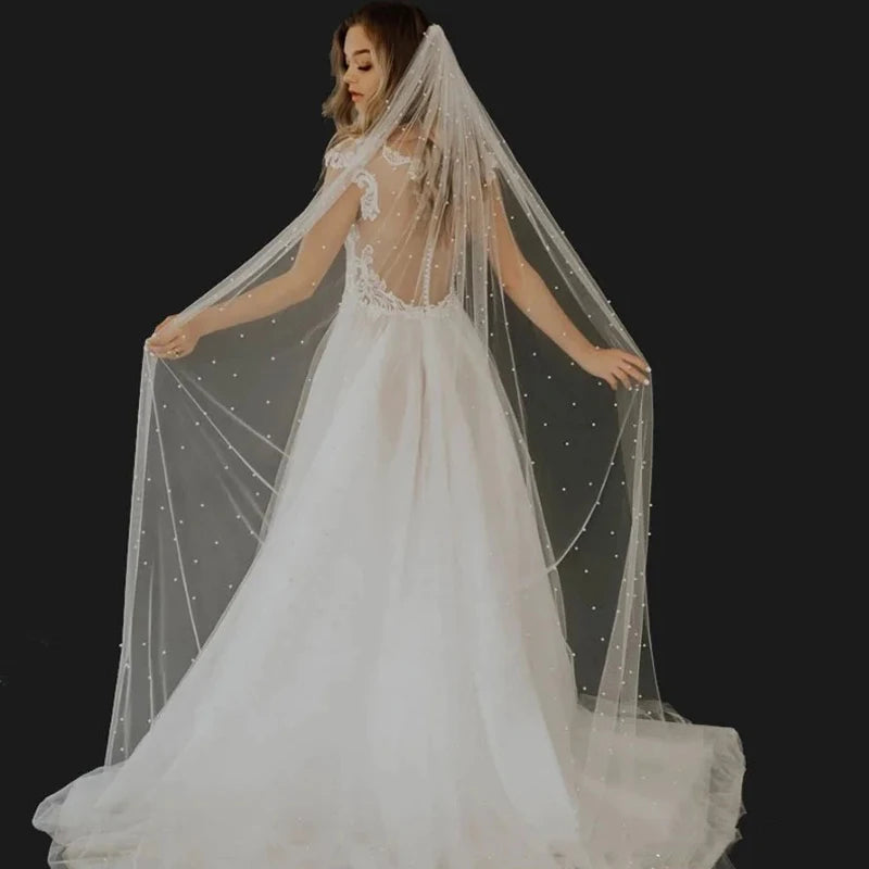 Una novia vistiendo un vestido de novia blanco y un velo transparente de perlas con peine.
