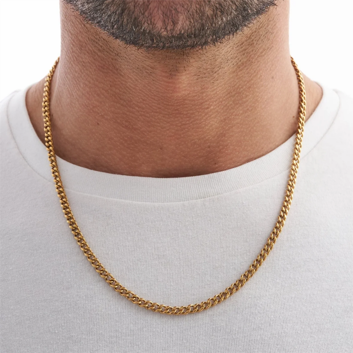 A close-up of a gold Cuban link chain necklace worn around the neck against a white shirt.