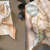 A light beige silk scarf with a floral print featuring soft peach and muted blue tones.