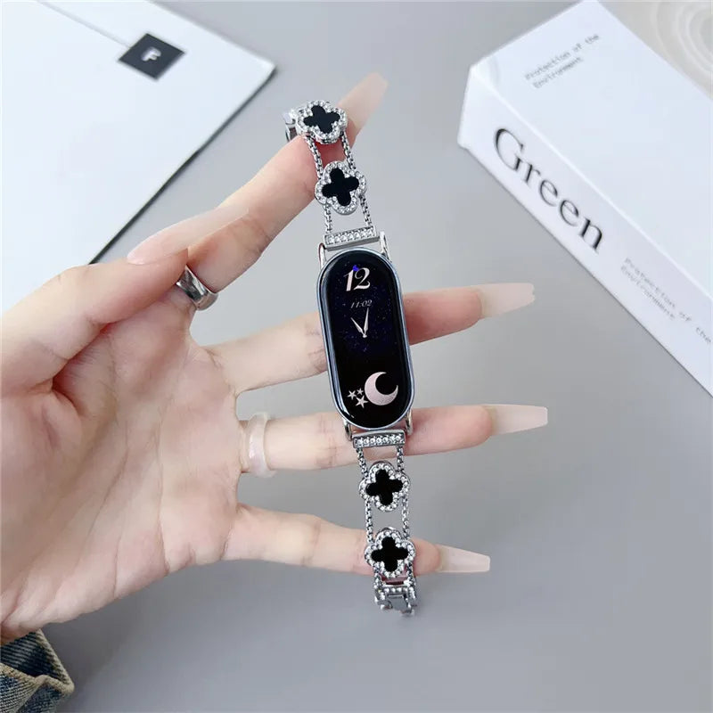 A hand holds a black digital watch with a silver strap featuring diamond four-leaf clovers and a crescent moon.