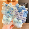 A hand holds a cluster of light blue and lavender sheer fabric flower bow hair ties.