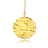 A gold skull pendant necklace with a chain, displayed on a reflective surface.