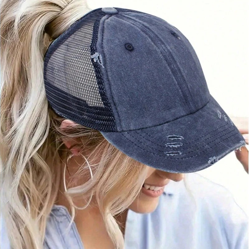 A woman is wearing a dark blue vintage mesh baseball cap with a light blonde hairstyle.