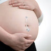 A close-up of a pregnant belly showing two silver belly button rings.