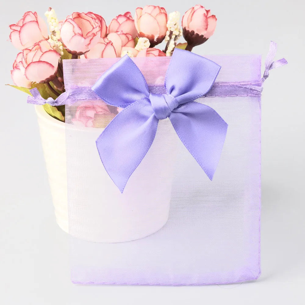 A purple organza drawstring gift bag tied with a lavender ribbon, filled with pink and white flowers.