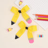 A set of yellow and pink pencil bow hair clips displayed on a white lined paper.