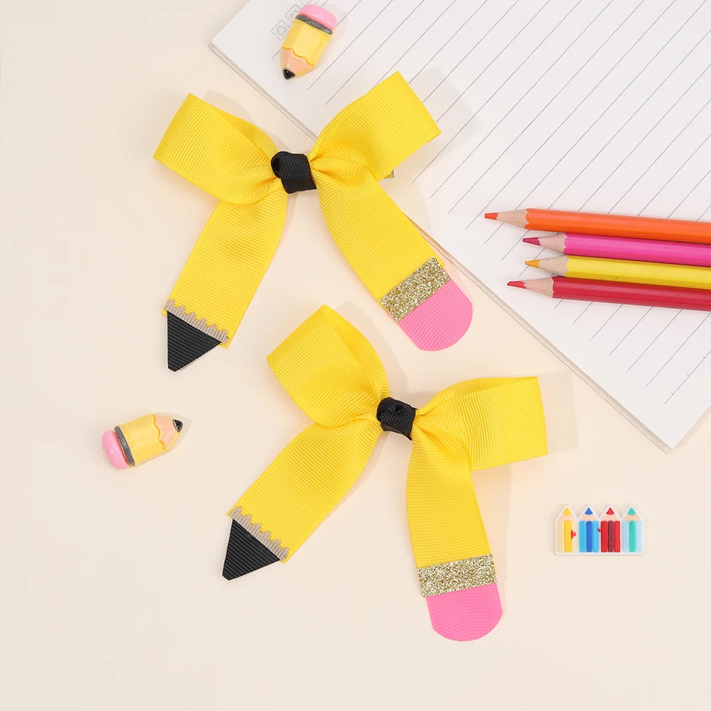 A set of yellow and pink pencil bow hair clips displayed on a white lined paper.