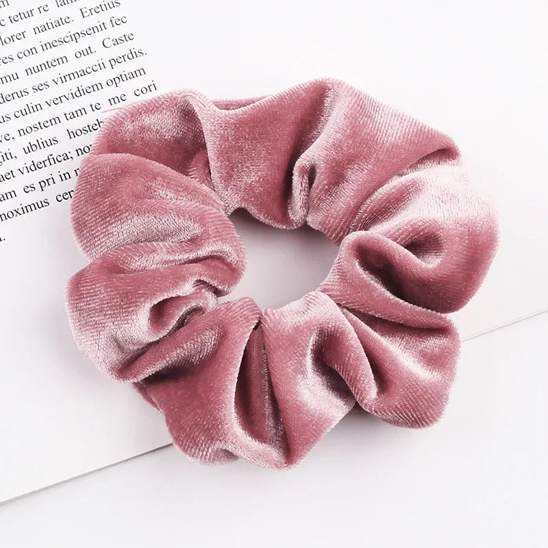 A close-up of a set of six dusty rose velvet scrunchies with gathered fabric texture resting on a white background.