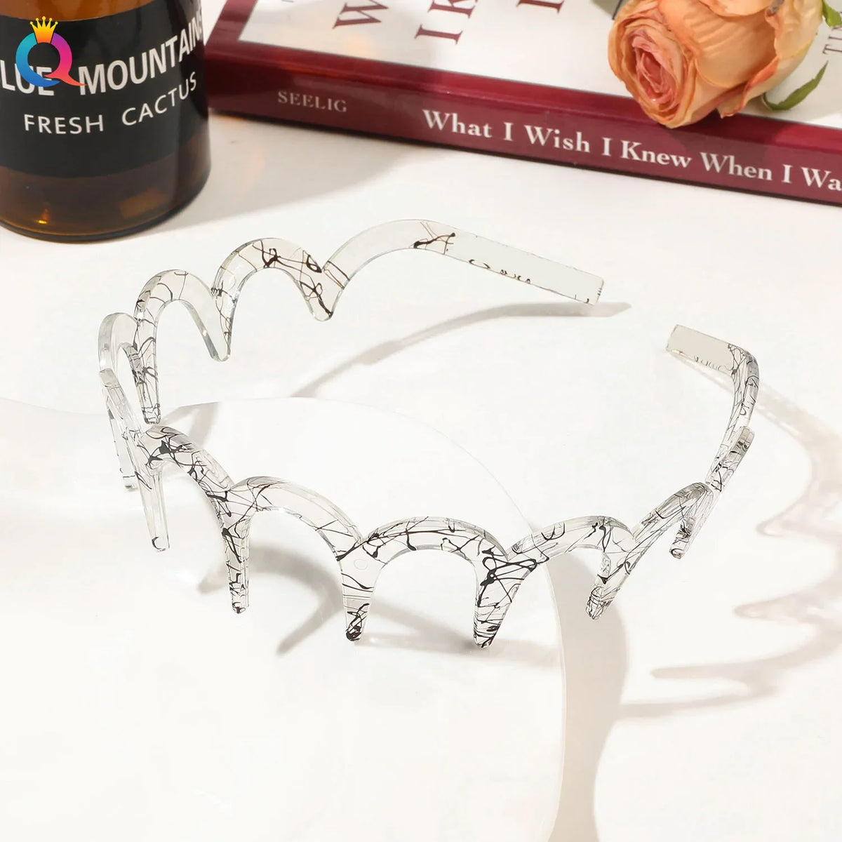 Clear acetate toothed headbands displayed on a white surface next to a book and a cactus bottle.