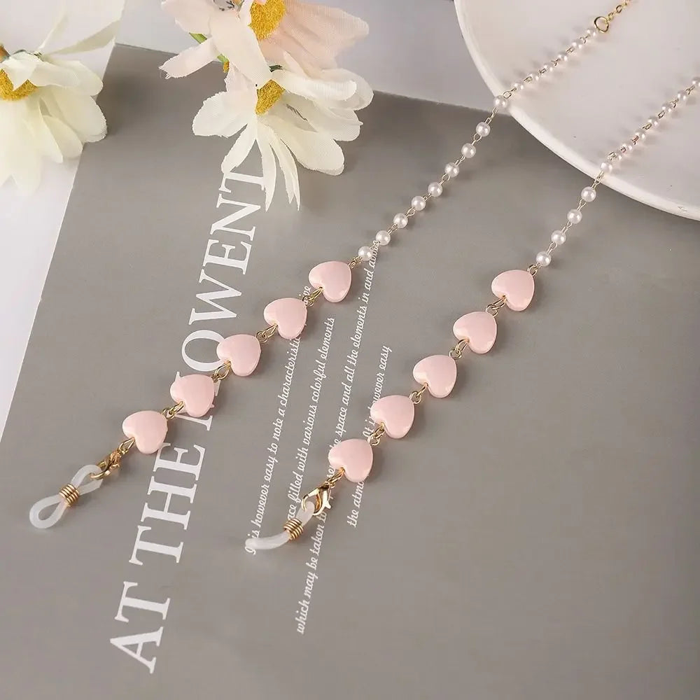A delicate pearl beaded eyewear chain with pink beads and gold accents displayed on a gray background.
