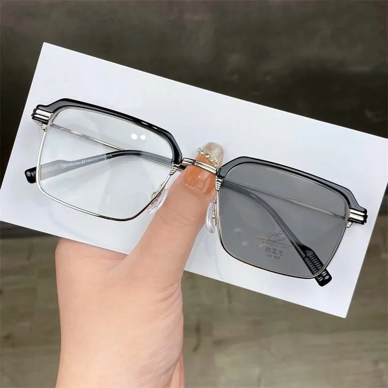 Eine Hand hält eine schwarze photochromische Brille mit klaren Linsen und UV-Schutz vor einem weißen Hintergrund.