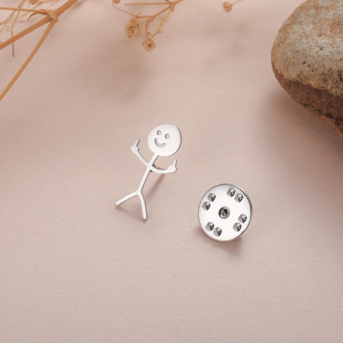 Silver punk stickman brooch and a round silver stud earring on a beige background