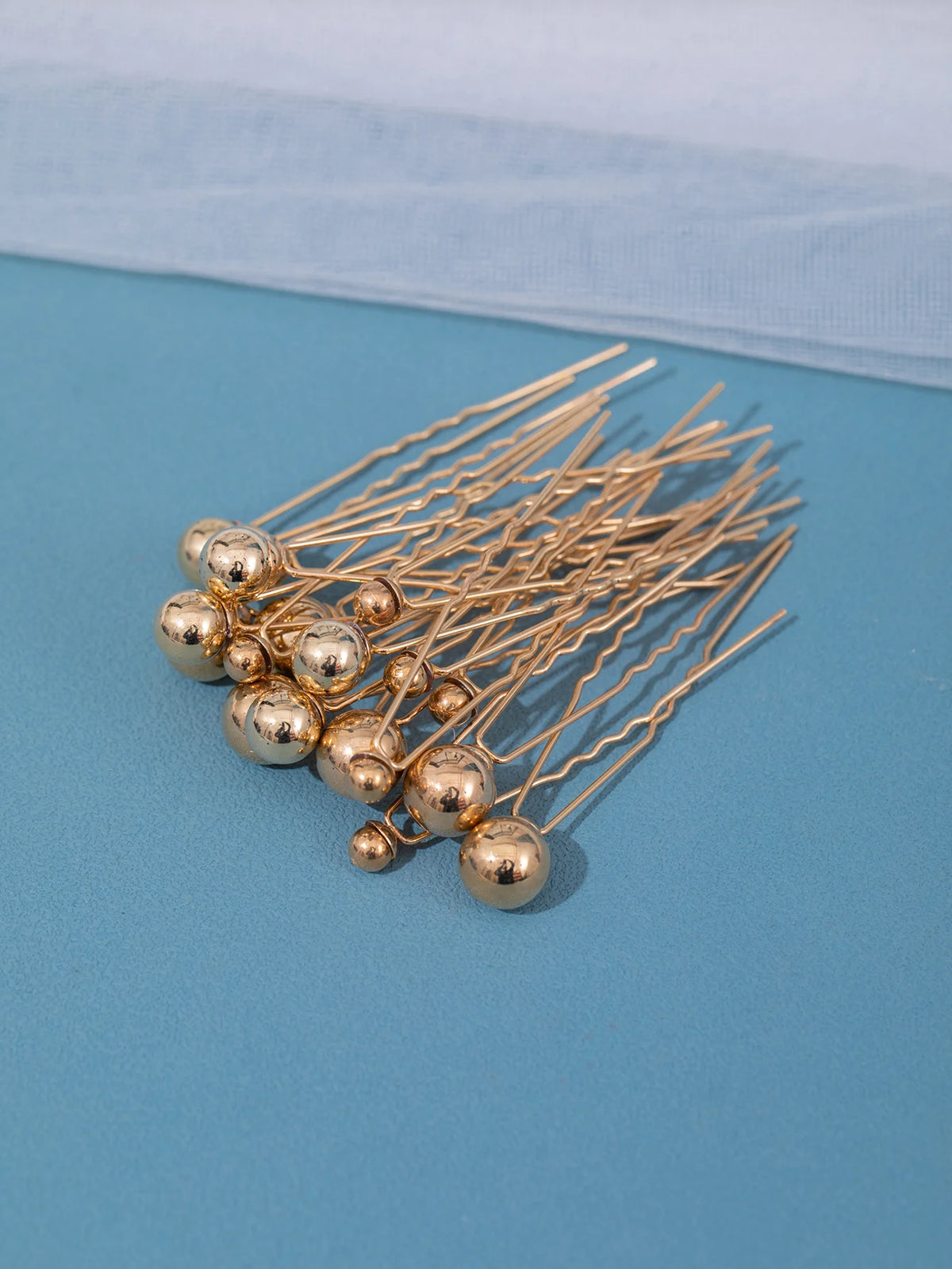 A cluster of 18 gold-toned faux pearl hair pins arranged on a light blue surface.
