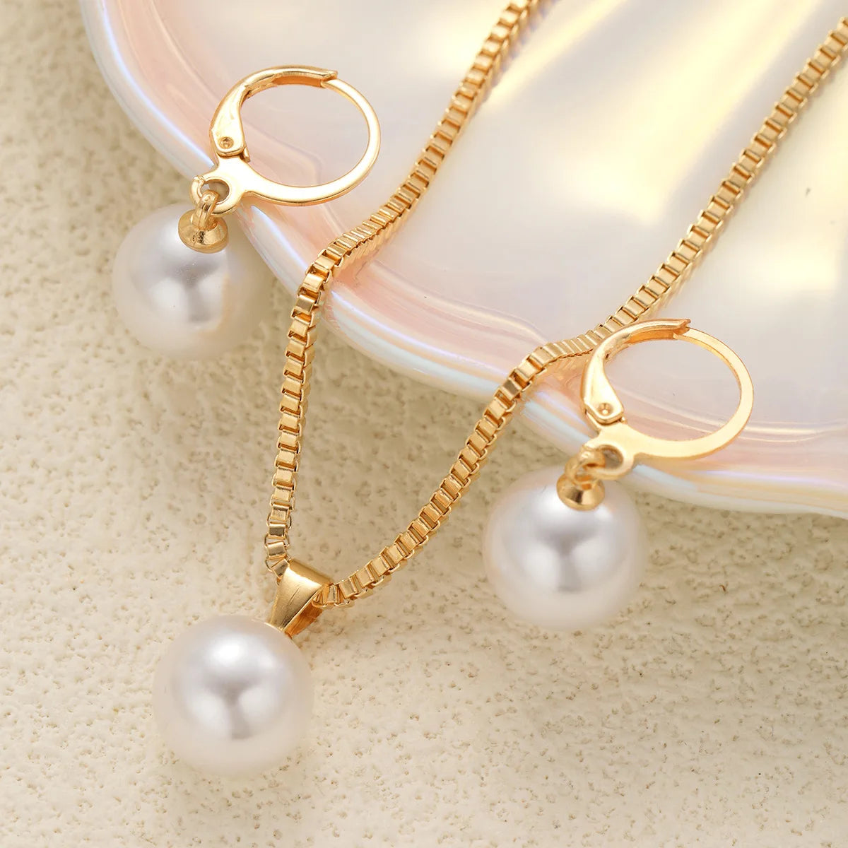 A set of dainty gold pearl jewelry featuring matching earrings and a delicate necklace displayed on a light surface.