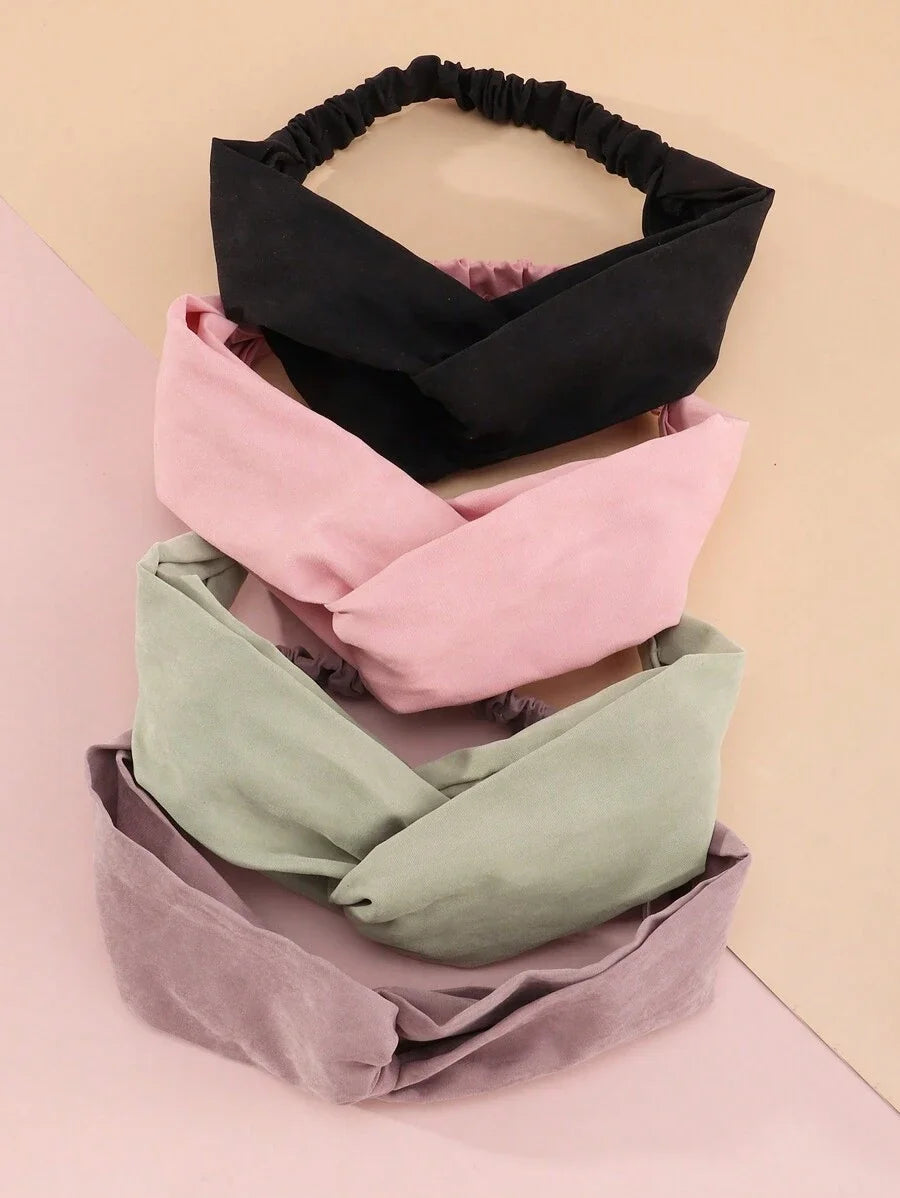 Ein Stapel von vier weichen Stoff-Haarbändern in Schwarz, Pink, Grün und Mauve.