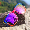 Gradient square frame polarized sunglasses resting on a rough rock with a blurred green background.