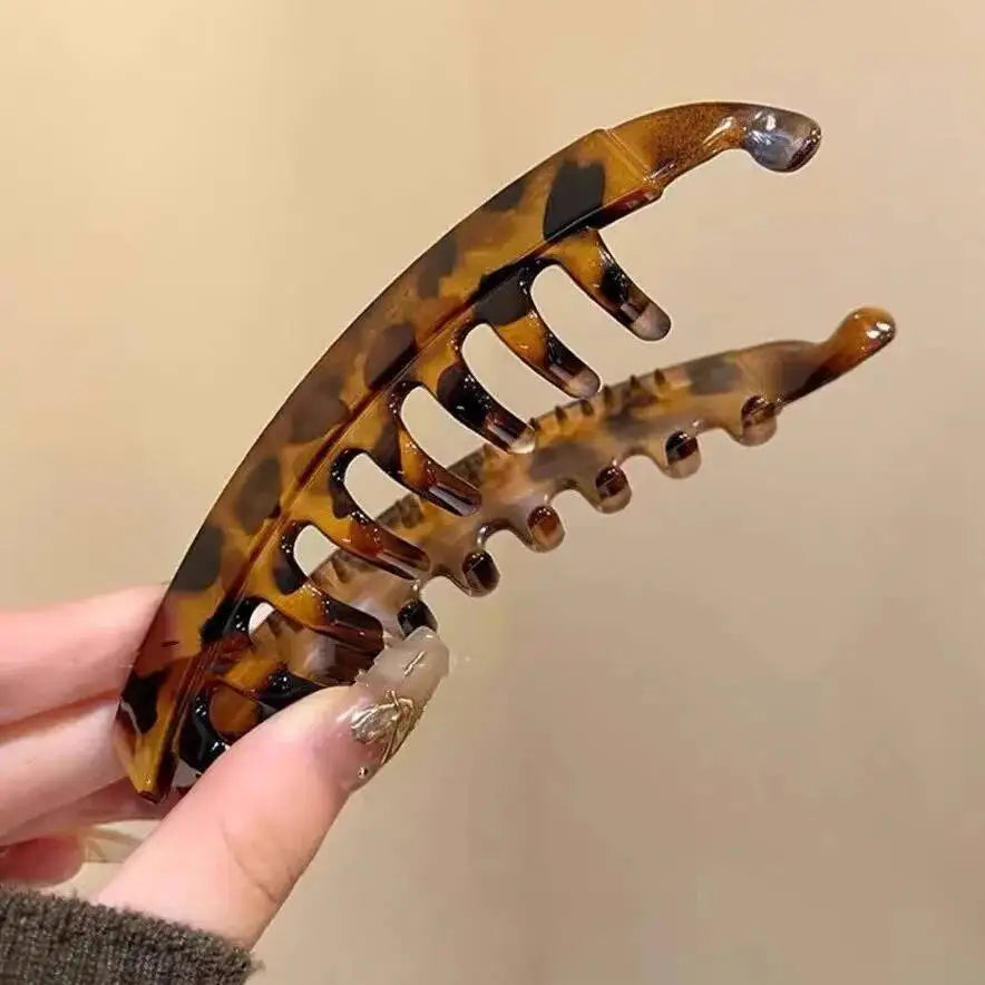 Ein Set aus Schildpatt-Bananen-Haarspangen und Haarspangen wird von einer Hand vor einem hellen Hintergrund gehalten.