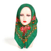 A woman wearing a deep green scarf with a floral print covering her head and neck.