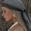 A woman wearing a gray shawl with black lace trim and a gold leaf earring.