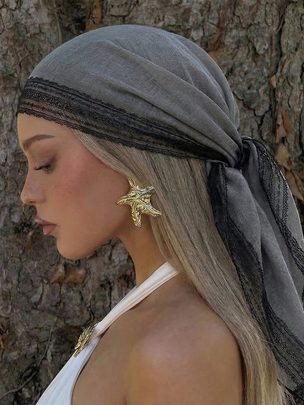 A woman wearing a gray shawl with black lace trim and a gold leaf earring.
