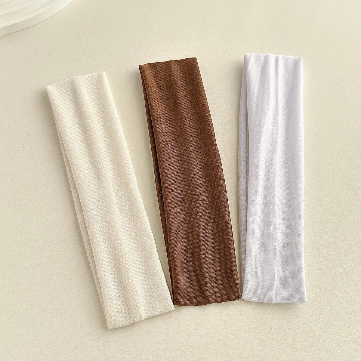 Three solid fabric headbands in cream, brown, and white displayed vertically on a light background.