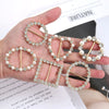 A hand holds several elegant rhinestone and pearl decorative button clips on a white background.