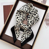 A black and white leopard print silk scarf tied in a bow displayed in a wooden frame.
