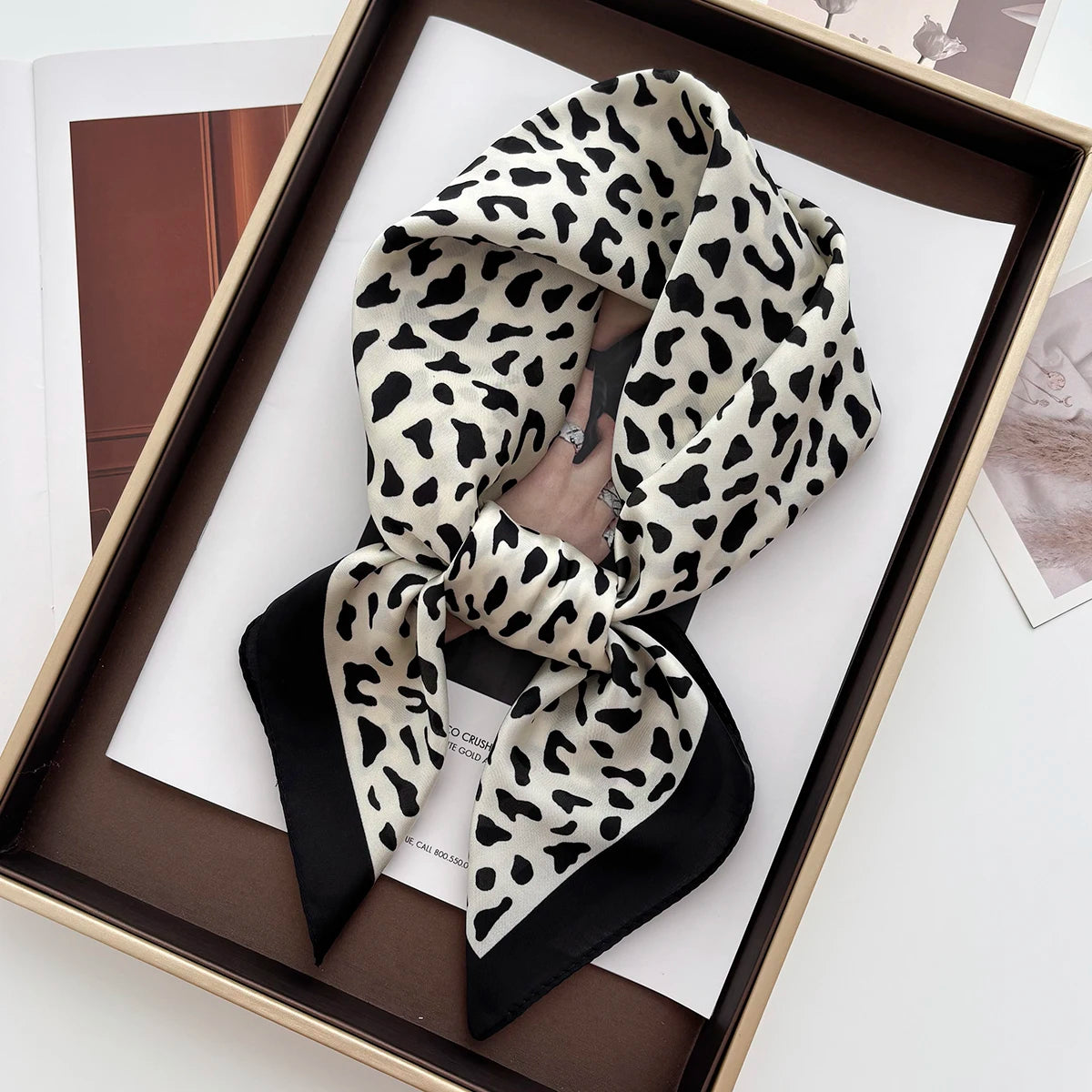 A black and white leopard print silk scarf tied in a bow displayed in a wooden frame.