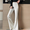 A woman wearing high-waist flare skinny white pants and a black top standing in front of a wooden panel.