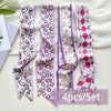 A set of four silk satin hair and bag accessories featuring purple and pink patterned ribbons.