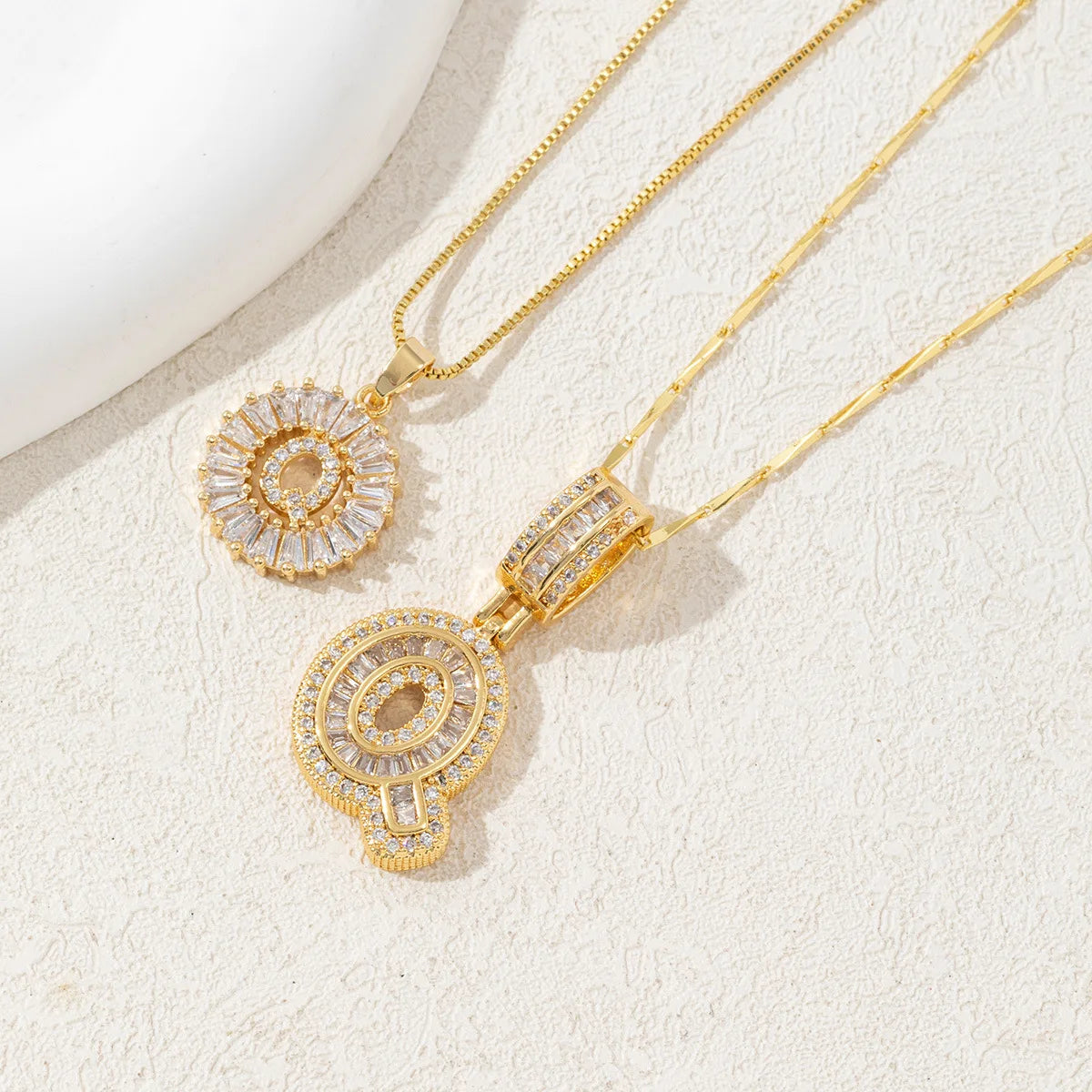 Gold-toned necklace set featuring CZ crystal pendants shaped like letters, displayed on a light background.