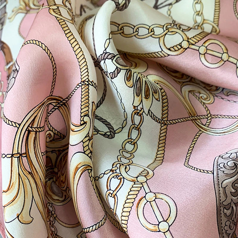A close-up of a pink silk print shawl featuring intricate gold and brown chain and vine patterns.