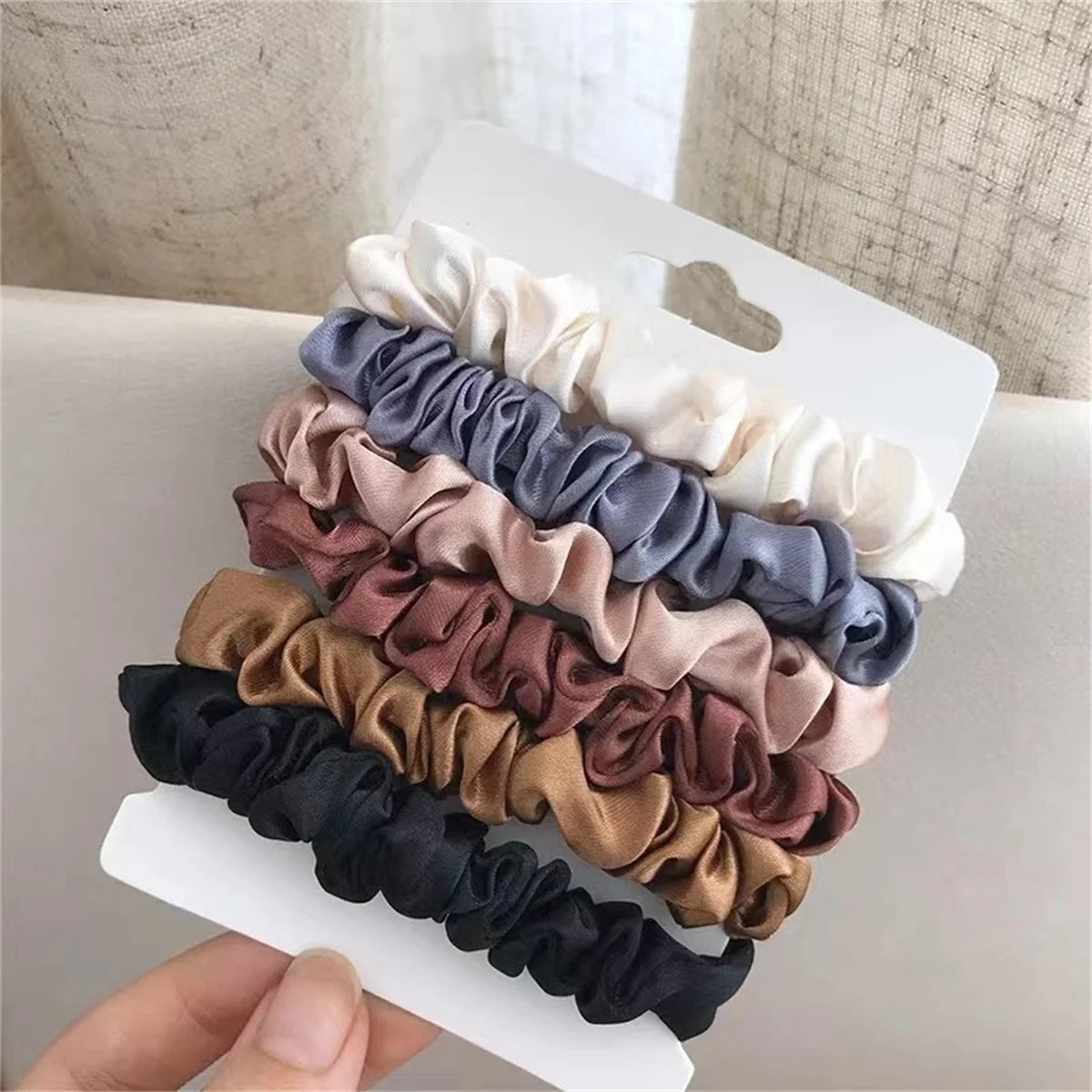 A pack of six satin hair scrunchies in various shades including beige, gray, mauve, brown, black, and cream.