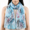 Écharpe de soie florale bleu clair avec des fleurs grises et roses drapée autour du cou d'une personne.