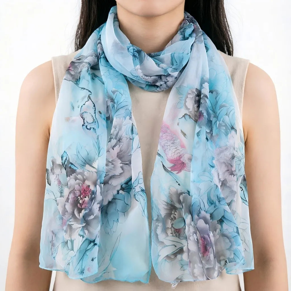 Écharpe de soie florale bleu clair avec des fleurs grises et roses drapée autour du cou d'une personne.