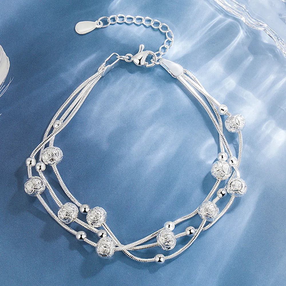 A silver bell bangle bracelet for women with intricate floral detailing and a chain closure.