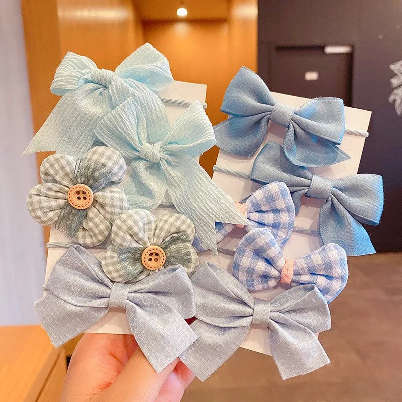 A collection of light blue and gray fabric flower bow hair ties for girls displayed on a white card.