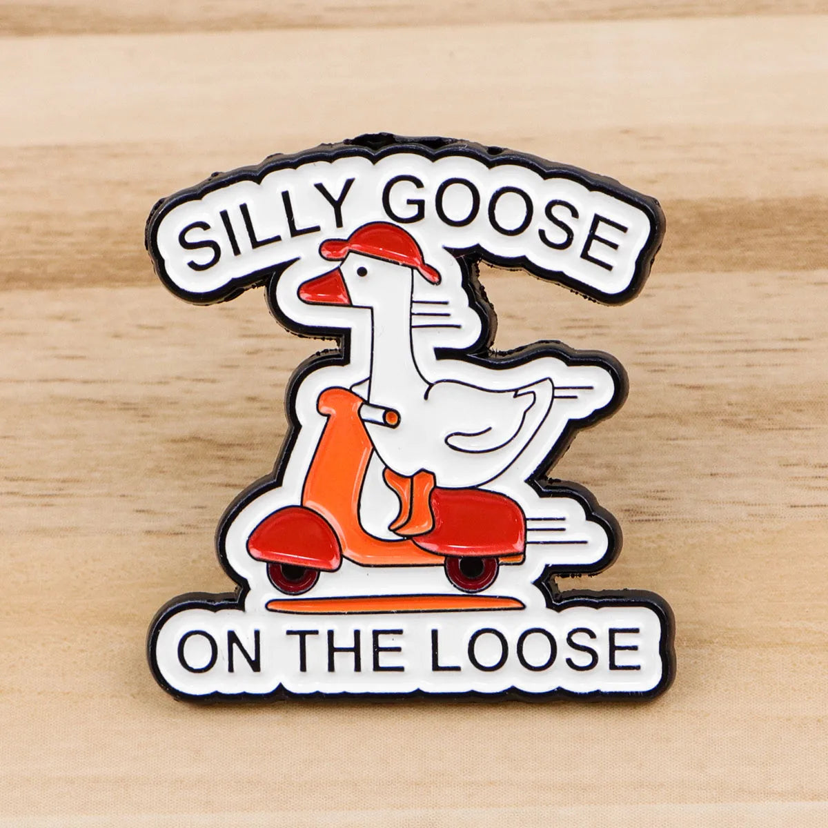 An enamel pin featuring a cartoon goose riding a scooter with the text Silly Goose On The Loose