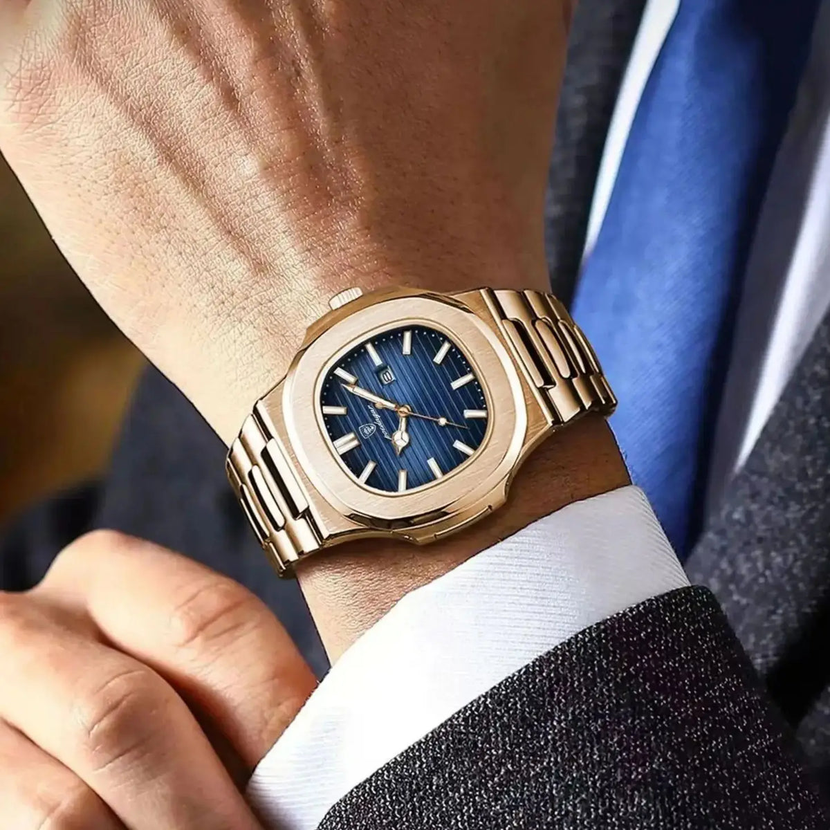 Nahaufnahme einer goldfarbenen Edelstahluhr mit blauem Zifferblatt und blauem Armband, getragen am Handgelenk neben einem Sak