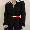 A woman wearing a black blazer and light blue shirt with an orange leather belt.