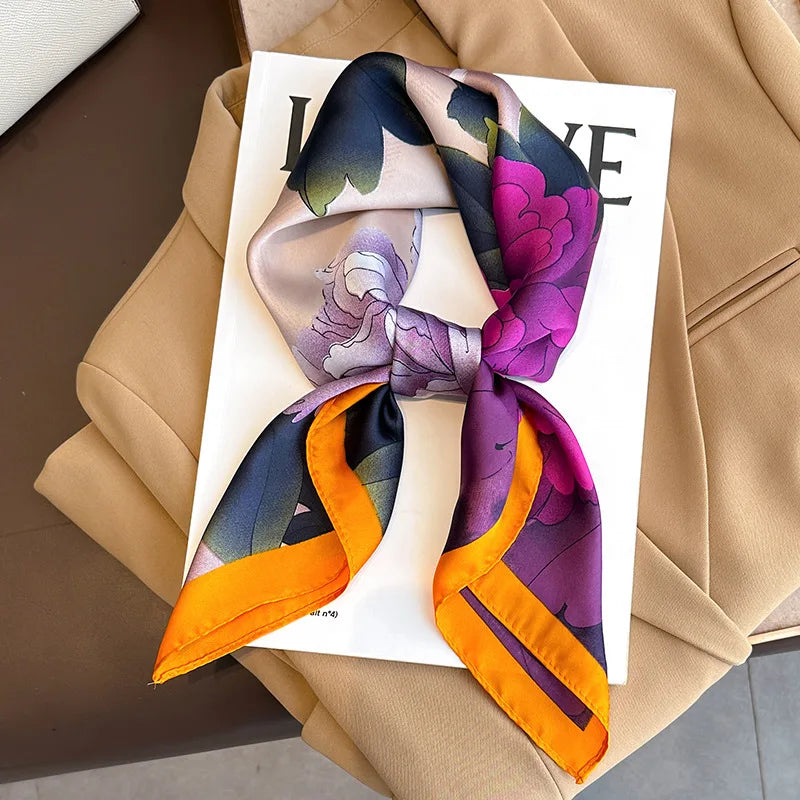 A luxury silk scarf featuring a floral pattern in shades of purple, pink, and orange tied in a square shawl.