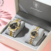 A pair of matching gold-toned watches with black dials and luminous hands displayed in a gray box.