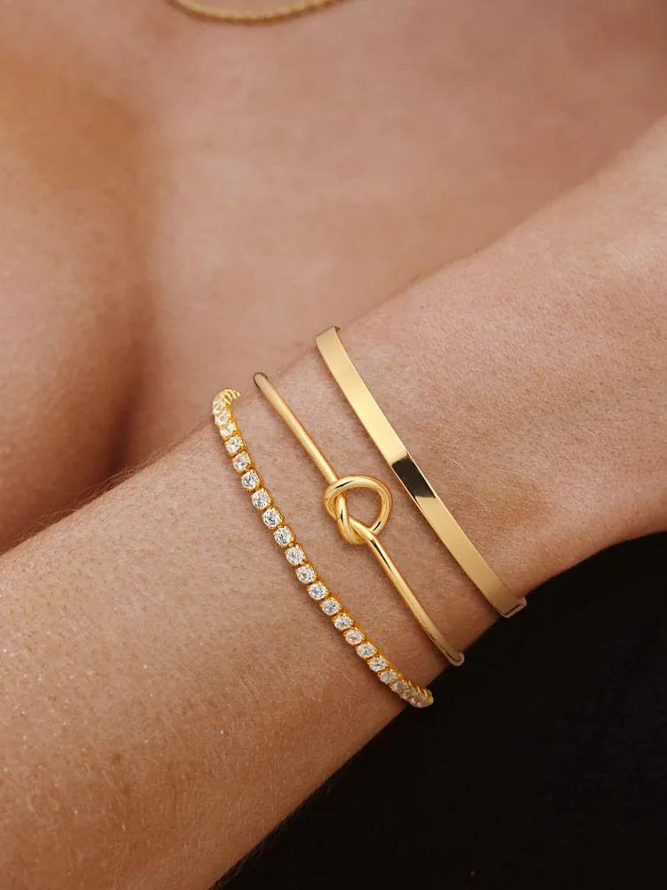 Three gold-plated stainless steel bracelets stacked on a woman's wrist.