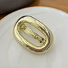 A gold-colored metal oval hair clip resting on a white plate.