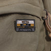 A black enamel pin featuring the word METAL and a cassette tape design on a canvas military green fabric.