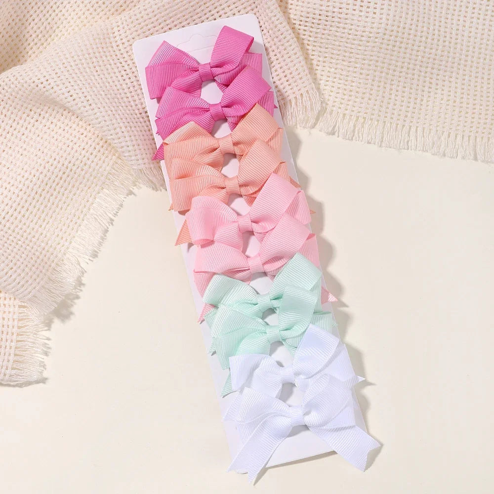 A collection of pink, peach, and mint green handmade ribbon bow hair clips displayed on a white card against a cream knitted 