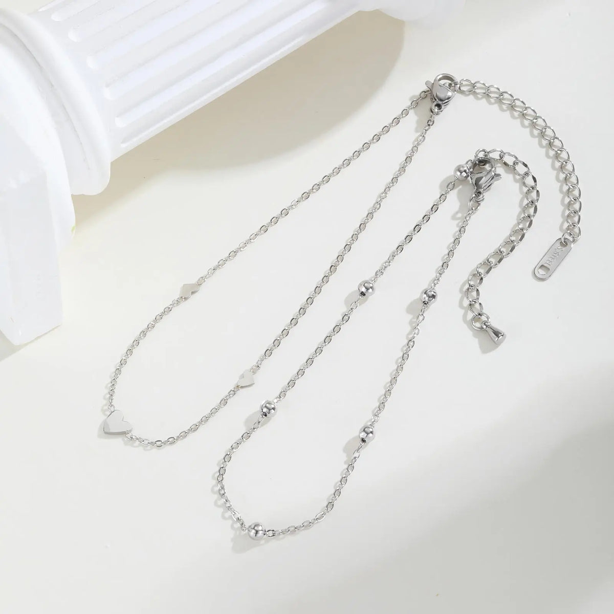 A set of stainless steel heart double chain anklets displayed on a white surface.