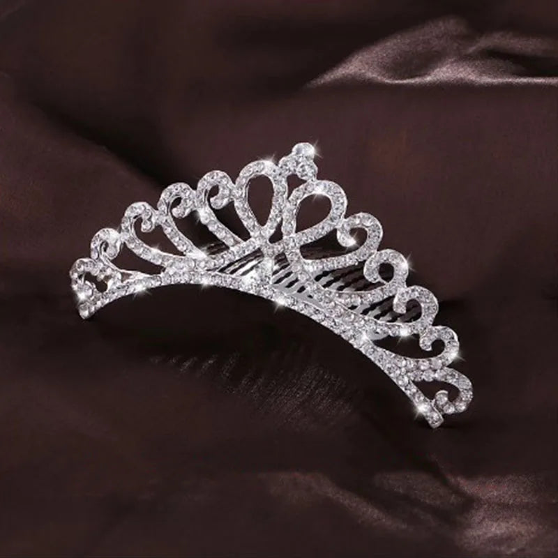 A sparkling crystal princess tiara hair comb for women is displayed against a dark brown fabric.
