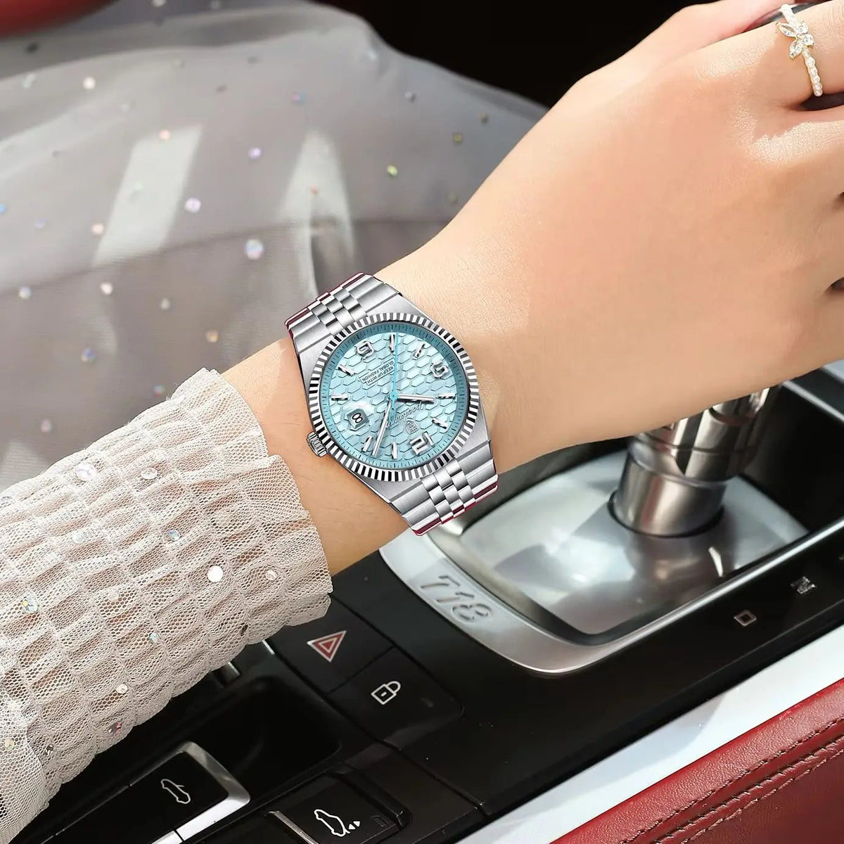 A close-up of a silver quartz wristwatch with a blue luminous dial and pink enamel accents on a woman's wrist.